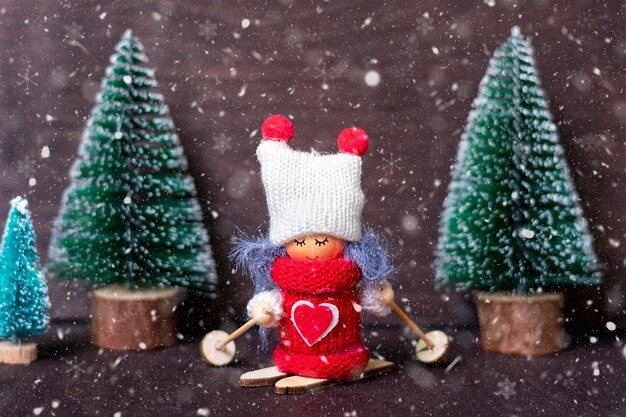 Winterkomposition Mädchen Skifahren in roten Kleidern und weißem Hut, Weihnachtsbaum auf hölzernem Hintergrund