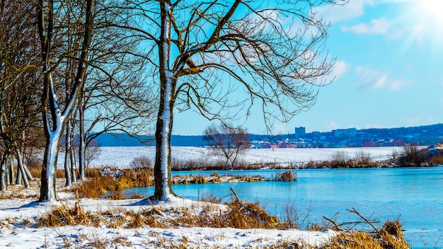 Winterlandschaft mit Fluss und Bäumen am Ufer bei sonnigem Wetter