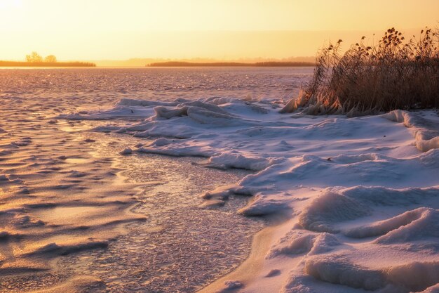 Winterlandschaft mit gefrorenem See und feurigem Himmel des Sonnenuntergangs. Zusammensetzung der Natur.