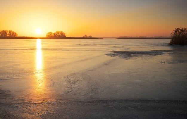 Winterlandschaft mit gefrorenem See und feurigem Himmel des Sonnenuntergangs. Zusammensetzung der Natur.