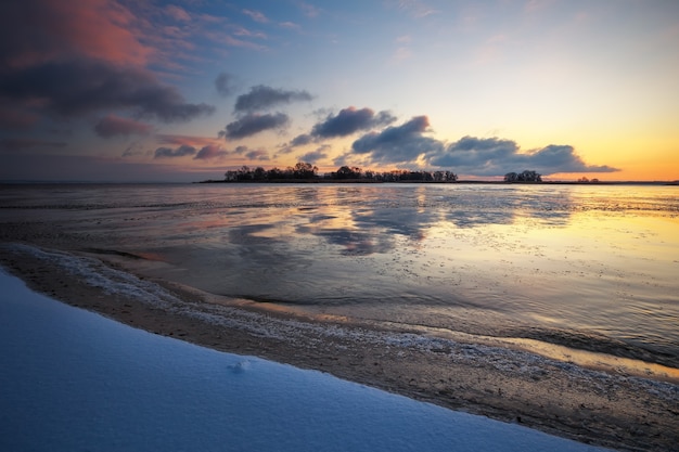 Winterlandschaft mit gefrorenem See und Sonnenunterganghimmel. Bunter orangefarbener Himmel. Zusammensetzung der Natur.