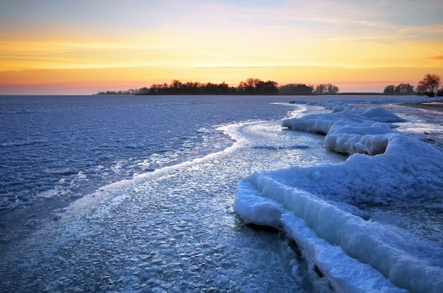 Winterlandschaft mit See und feurigem Himmel des Sonnenuntergangs. Zusammensetzung der Natur.