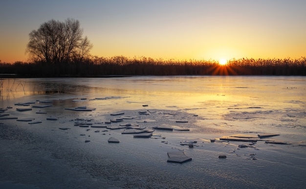 Winterlandschaft mit Sonnenunterganghimmel und gefrorenem Fluss. Tagesanbruch