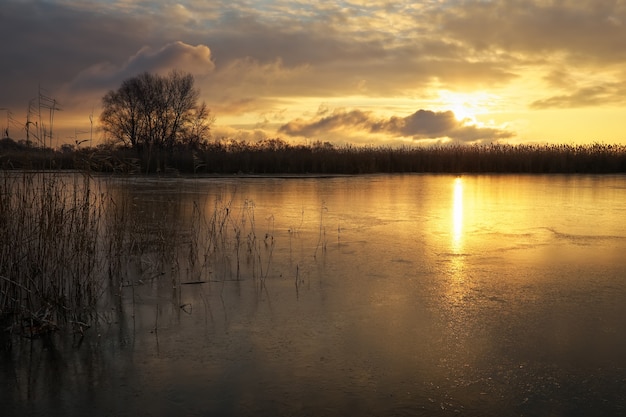 Winterlandschaft mit Sonnenunterganghimmel und gefrorenem Fluss. Tagesanbruch