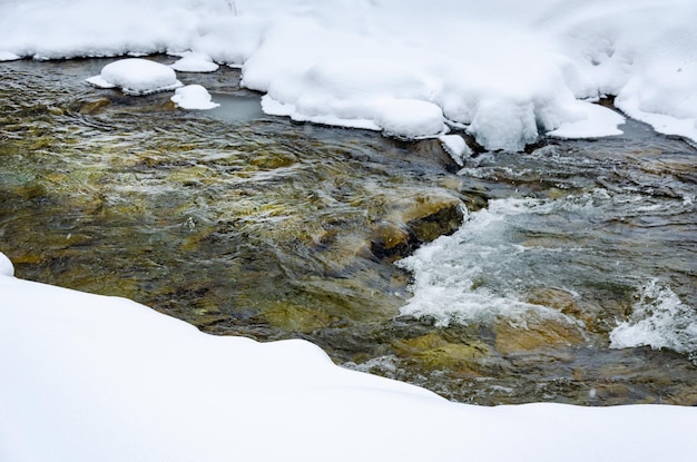 Winterliche Berglandschaft, gefrorener Fluss, bedeckt mit Schnee, der zwischen den Bäumen fließt