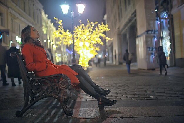 Winternacht in den Lichtern der Stadt / erwachsenes Mädchen in einem Mantelspaziergang in der Stadt, modisches stilvolles Bild eines schönen Modells