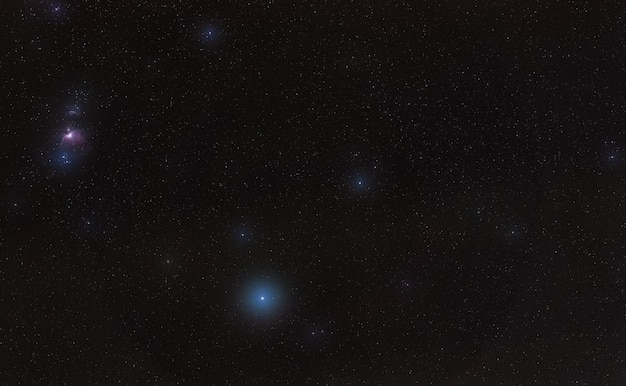 Winternachthimmel mit purpurfarbenem Orion-Nebel und hellblauem Rigel-Stern, der durch einige Wolken im unteren unteren Teil des Long Exposure-Fotos diffundiert ist