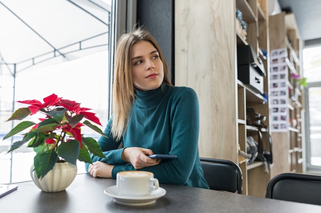 Winterporträt der Frau, die am Café mit Tasse Kaffee sitzt