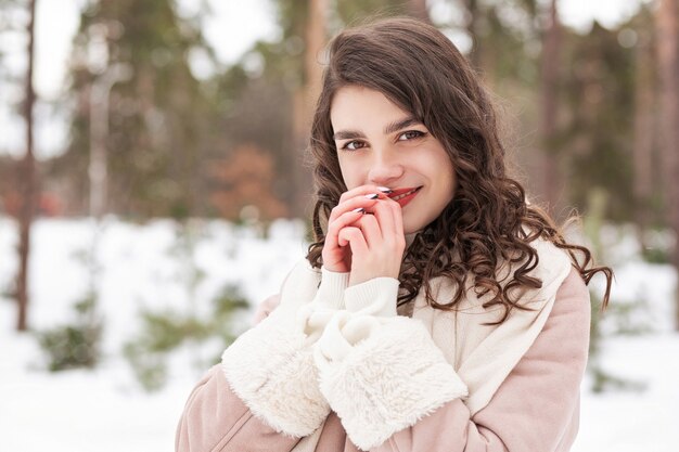 Winterporträt einer fröhlichen brünetten Frau trägt Schal und warmen Mantel, die im Wald spazieren gehen. Freiraum
