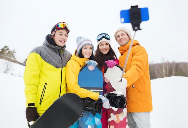 wintersport, freizeit, freundschaft, technologie und menschenkonzept - glückliche freunde mit snowboards und smartphone, die selfie machen