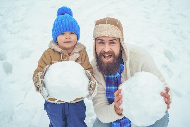 Wintervater und -sohn spielen im Freien glückliches Kind, das mit Schneeball gegen weißen Winterhintergrund spielt