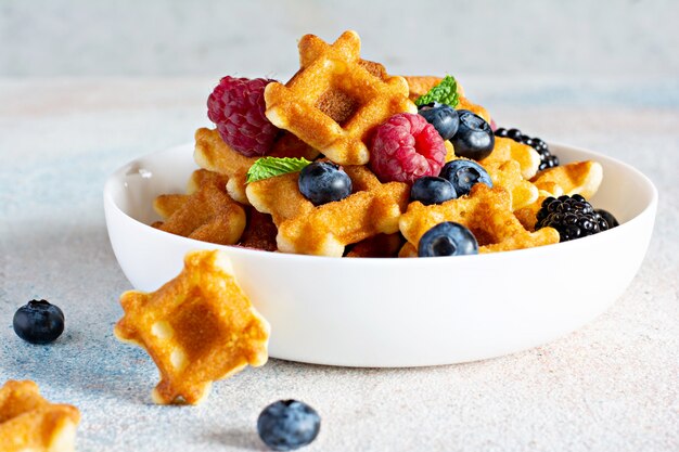 Winzige (Mini) Waffeln zum Frühstück mit Beeren in einer weißen Schüssel auf Weiß