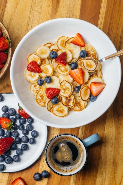 Winzige Pfannkuchen zum Frühstück. Pfannkuchen mit Erdbeeren und Blaubeeren, die morgens zum Frühstück in der Wohnküche gekocht werden.