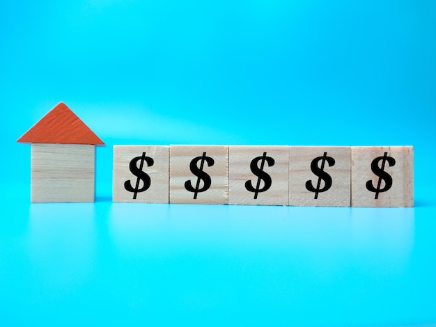 Winziges Haus und Holzwürfel mit Währungssymbol auf blauem Hintergrund