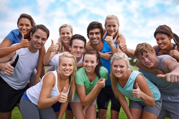 Wir haben einen unterhaltsamen Weg gefunden, um gesund zu bleiben Eine Gruppe glücklicher junger Menschen, die auf einem Sportplatz stehen und der Kamera den Daumen hochgeben