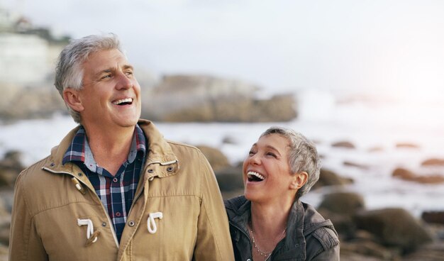 Wir haben immer die besten Lacher zusammen geteilt Aufnahme eines schönen älteren Paares, das am Strand spazieren geht