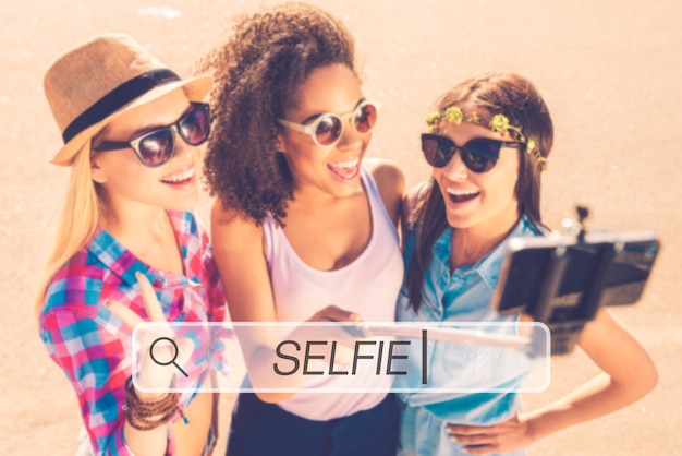 Wir lieben Selfies! Draufsicht auf drei junge glückliche Frauen, die mit ihrem Smartphone Selfie machen, während sie zusammen im Freien stehen