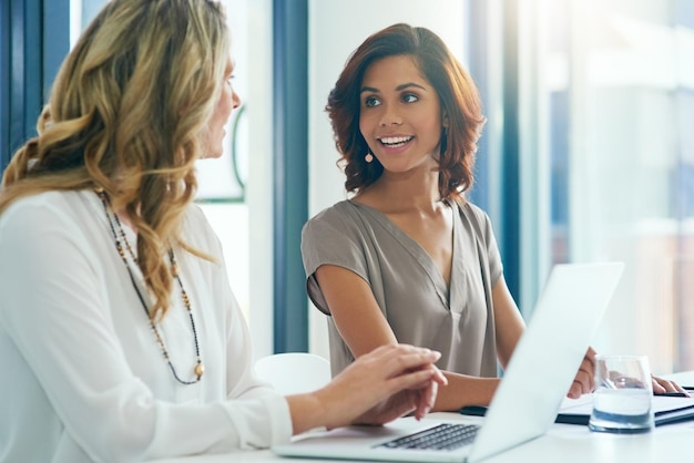 Wir machen wirklich Fortschritte Aufnahme von zwei Geschäftsfrauen, die sich unterhalten, während sie einen Laptop benutzen