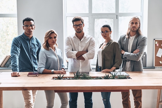 Wir sind das beste Team! Gruppe junger moderner Menschen in intelligenter Freizeitkleidung, die im Kreativbüro in die Kamera schaut