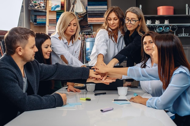 Wir sind ein Team. Erstaunliche kreative Gruppe erfolgreicher Büroangestellter, die als Zeichen der Motivation und Unterstützung ihre Hände in einer kreativen Umgebung übereinander legen. Konzept der Teamunterstützung