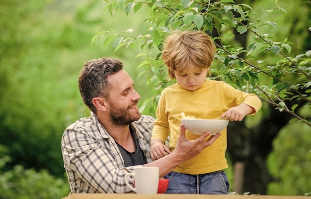 Wir sind eine Familie Frühstück am Morgen Vegetarische Ernährung Familienessen glücklicher Vatertag Kleiner Junge mit Papa isst Müsli gesunde Ernährung und Diät Milchprodukte Vater und Sohn essen im Freien