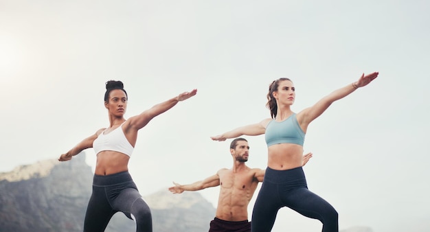 Wir sind Krieger Schnappschuss von drei jungen Menschen, die in Kriegerhaltung stehen, während sie am Strand Yoga machen