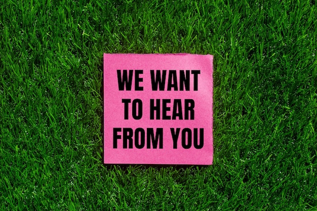 Wir wollen von Ihnen eine Nachricht hören, die auf zerrissenen rosa Papier mit grünem Gras-Hintergrund geschrieben ist.