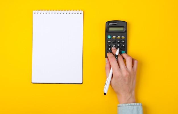 Wirtschaftliche Analyse. Weibliche Hände benutzen Taschenrechner auf einem Gelb mit einem Notizbuch