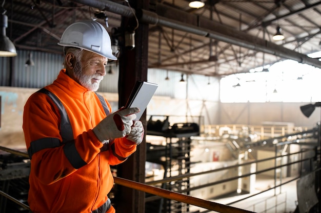 Wirtschaftsingenieur, der auf einer Metallplattform steht und die Produktion auf einem Tablet-Computer überprüft