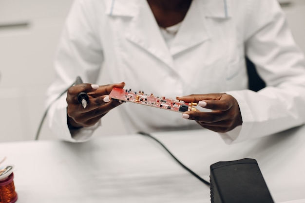 Wissenschaftler afroamerikanische Frau, die im Labor mit Lötkolbenforschung und -entwicklung von elektronischen Geräten nach Farbe schwarze Frau arbeitet