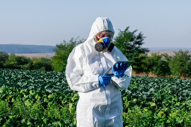 Wissenschaftler, die eine weiße Schutzausrüstung, eine chemische Maske und eine Brille tragen, verwenden Tabletten auf dem Feld der Farm.