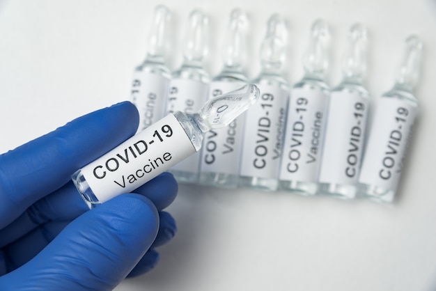 Wissenschaftlerhand in blauen Nitrilhandschuhen mit Ampullenhalteimpfstoff gegen Covid-19-Infektionskrankheit. Coronavirus heilen