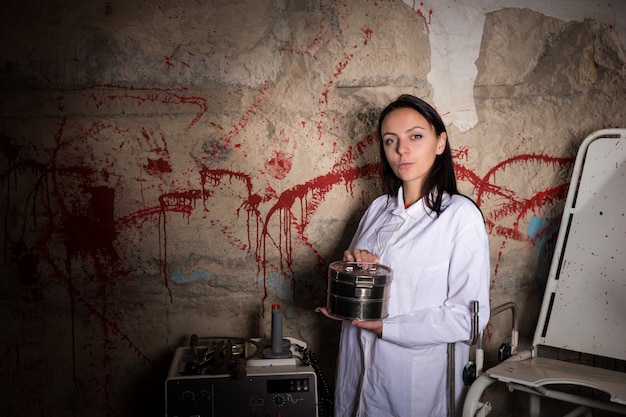 Wissenschaftlerin, die eine Aluminiumbox vor einer blutbespritzten Wand hält, Halloween-Konzept