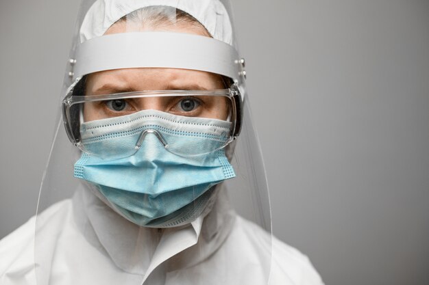 Wissenschaftlerin in Schutzkleidung mit Schild und medizinischer Maske.