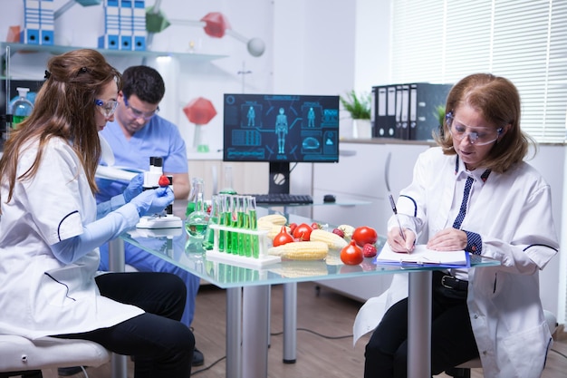 Wissenschaftlerin mittleren Alters, die sich nach einem Produkttest an Erdbeeren Notizen macht. Reagenzgläser.