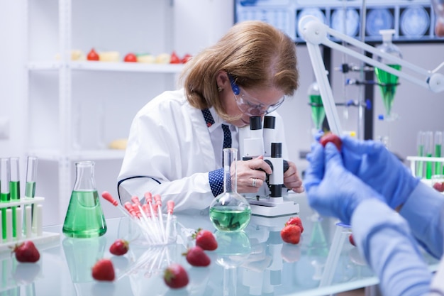 Wissenschaftlerin mittleren Alters mit Schutzbrille, die ihr Mikroskop untersucht. Forschungslabor.