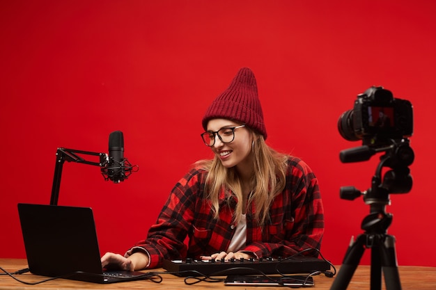 Woan sonriente joven sentada en la mesa y usando la computadora portátil que dispara su blog musical