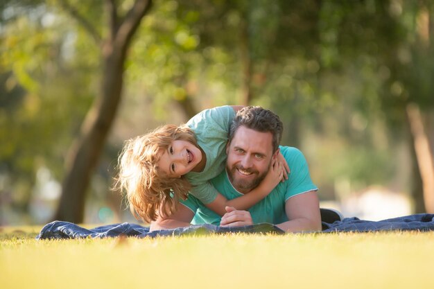 Wochenendaktivität Happy Family Lifestyle-Konzept Vater und Kind umarmen und umarmen sich im Freien Vater und Sohn legen sich im Sommerpark auf Gras und verbringen Zeit im Freien