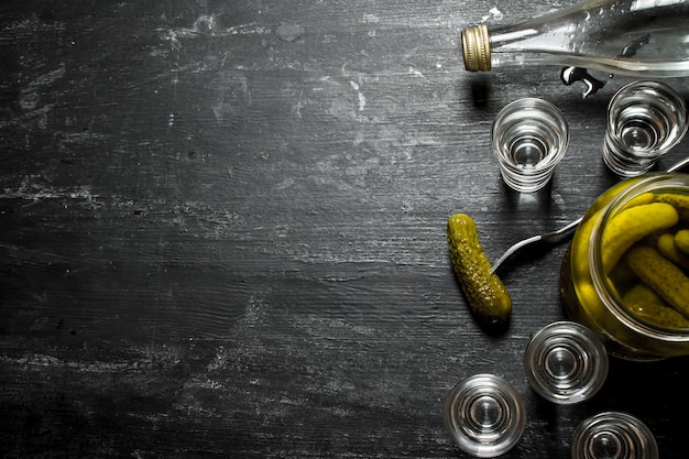 Wodka mit eingelegten Gurken auf schwarzem Holztisch.