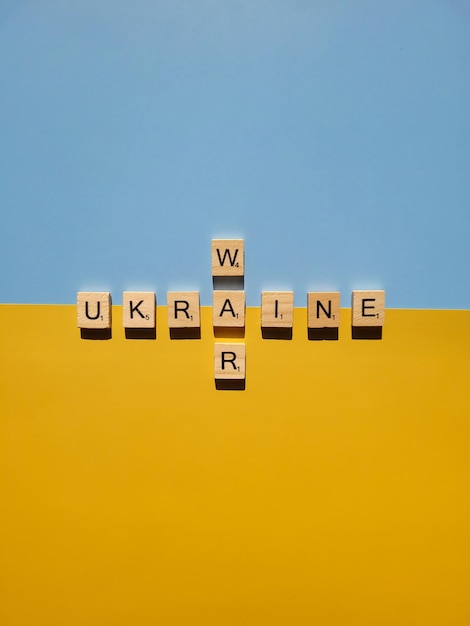 Wörter auf hölzernen Alphabetbuchstaben auf gelbem, blauem Hintergrundabschluß oben. Flach liegen. Unterstützung der Ukraine. Krieg