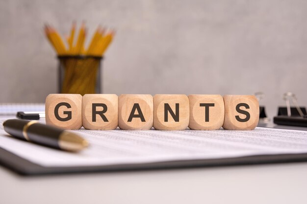 Wörter GRANTS auf Holzblöcken mit Büroartikeln im Hintergrund