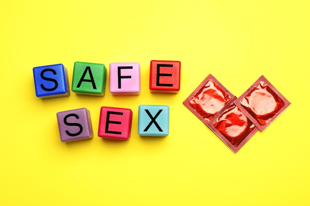 Foto wörter sicherer sex mit bunten würfeln und kondomen auf gelbem hintergrund flach gelegt