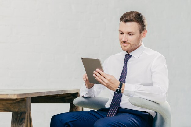 Wohlhabender gutaussehender Mann passt Webinar online auf modernem Tablet-Computer auf