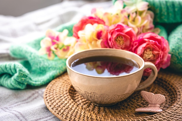 Wohnkomposition mit einer Tasse Teeblumen und einem Strickelement im Bett