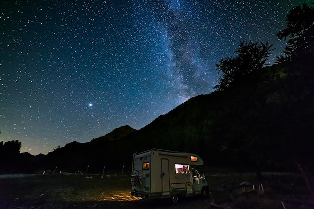 Wohnmobil unter Panorama-Nachthimmel in den Alpen Der Milchstraßenbogen und Sterne über beleuchtetem Wohnmobil Campingfreiheit in einzigartiger Landschaft