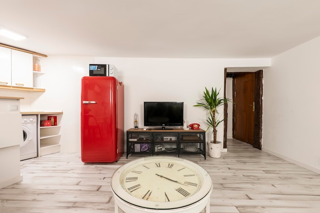 Wohnzimmer mit rundem Esstisch aus Holz, Kochnische in einer Ecke, Fernseher über Sideboard im Industriestil und antikem roten Kühlschrank