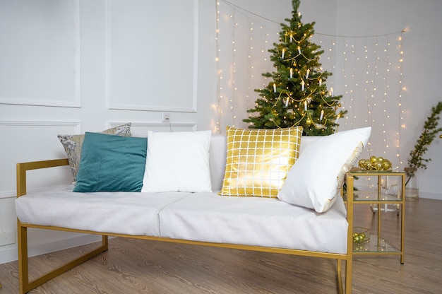 Wohnzimmer mit Sofa und großem Weihnachtsbaum und Kopienraum über weißer Wand mit Lichtern. Innenraum des neuen Jahres.