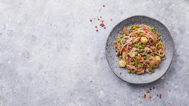 Wok con carne de pavo fideos soba maíz guisantes judías verdes y zanahorias servido sobre fondo gris