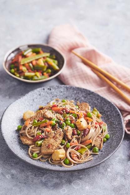 Wok con carne de pavo fideos soba maíz guisantes judías verdes y zanahorias servido sobre fondo gris