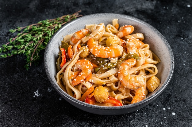 Wok chino Salteado de fideos de marisco udon con camarones y gambas en un bol. Fondo negro. Vista superior.